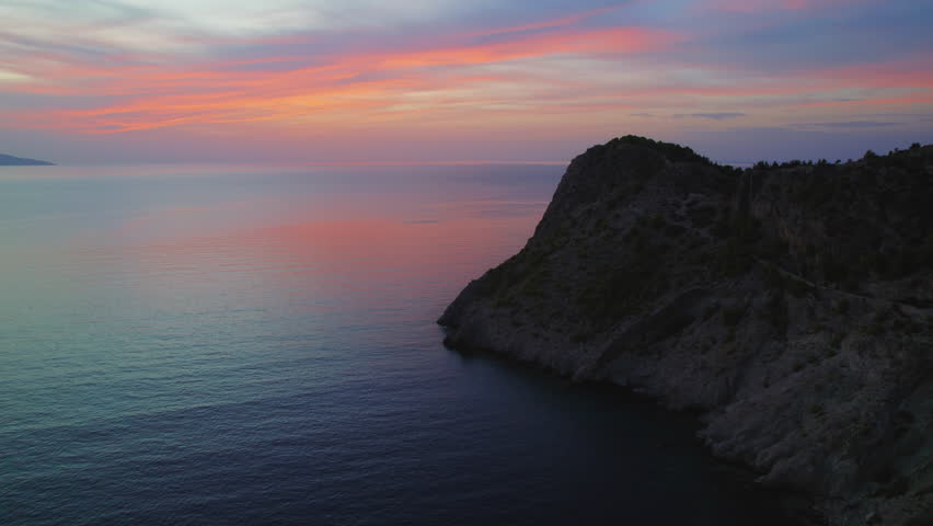 Dramatic sunset colors reflecting over calm sea beside rugged Kefalonia cliffs in evening light