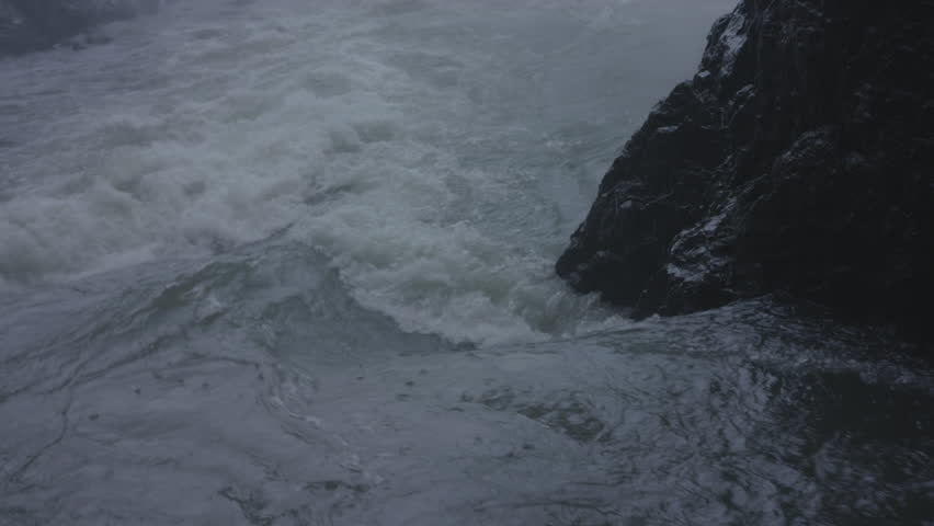 Close up of powerful, turbulent water flowing rapidly around a snowy rock formation