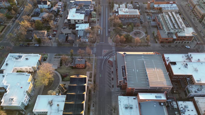 Marked intersection and small park over Boulder neighborhood near Pearl Street, mixed residential commercial buildings at sunrise. Flat roofs, asphalt markings, parked cars, sparse tree canopies. USA