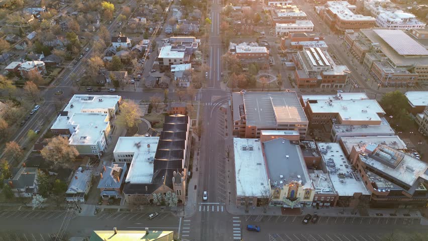 Central Boulder blocks blend small homes with multi story commercial buildings near Pearl Street and Spruce Street intersections. White roofs, brick facades, crosswalks, leafless trees contrast. USA