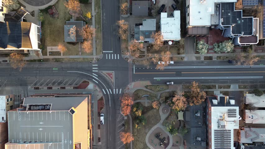 Crossroads with mixed blocks along Boulder Pearl Street form small homes, commercial buildings, marked parking lot. Soft evening light white rooftops, asphalt lines, sparse foliage, parked cars. USA