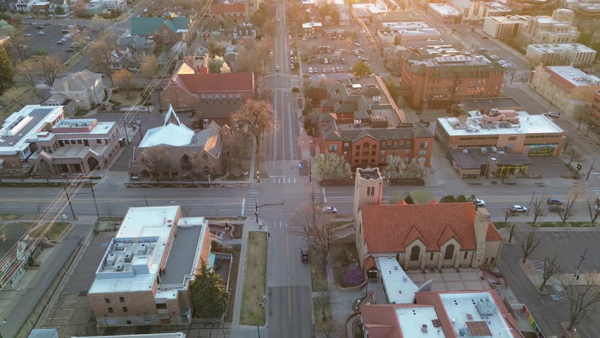Central Boulder streets meet near Pearl Street with red tiled roofs, church spires, mixed commercial buildings glowing under golden hour light. HVAC units, white rooftops, early foliage, Colorado. USA