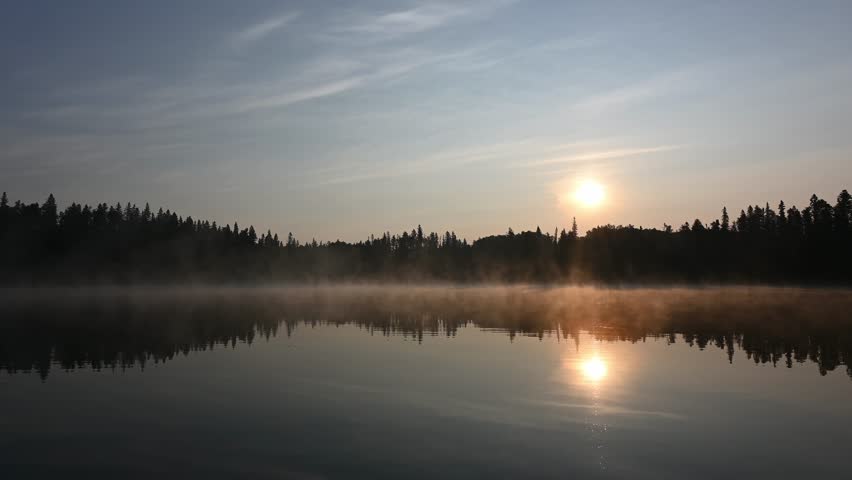 View Across a Calm Northern Park Lake as Morning Sun Lights Up Mist Over a Peaceful Reflective Water Landscape.