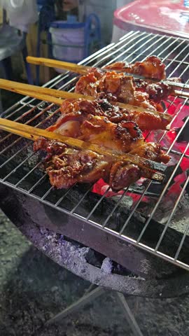 Vendor cooking Gay Yang (char-grilled marinated chicken) on street of Pattaya. Traditional thai street food at local night market. Vertical footage