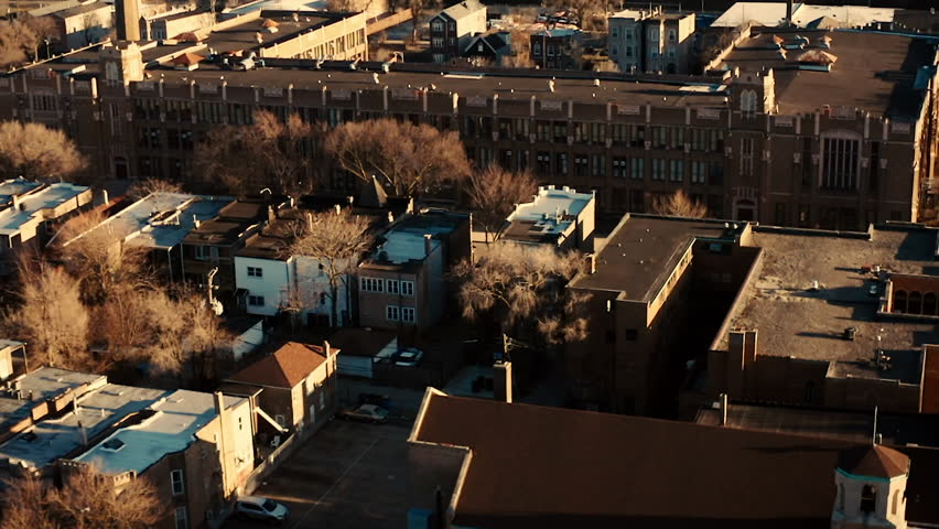 Aerial footage slowly orbiting an old, large brick school in a city neighborhood during sunset