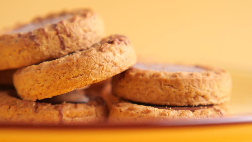 Close up motion footage of round cookies stacked on plate with yellow background.