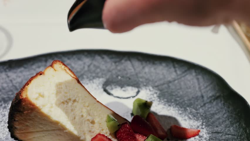 Sweet caramel sauce pouring over fresh basque cheesecake with strawberries and kiwi in slow motion.