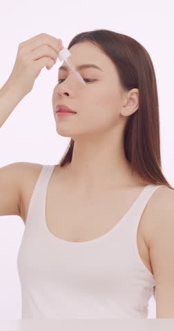 Young woman is using a dropper to apply skin serum to her face.