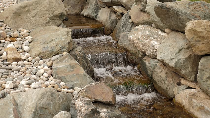 A picturesque waterfall cascading over rocks and plants in a stunning park. A man-made waterfall and a pond in a classic Japanese garden.