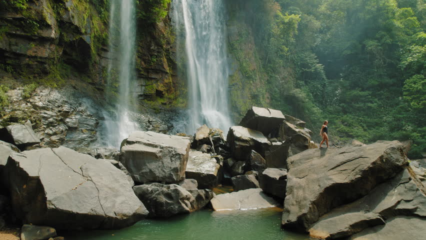 Bold woman walking on rocks near falling water of Nauyaca waterfall in Costa Rica