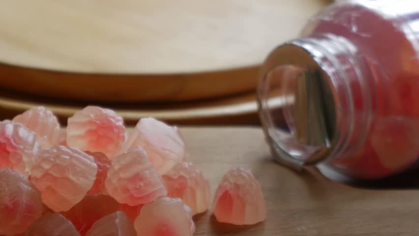 Macro close-up of translucent pink red flower-shaped health gummy vitamin supplement candy piled on wooden surface with warm bokeh