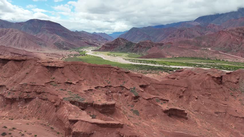 Aerial view of majestic red rock mountain formations with green vegetation under a cloudy sky.