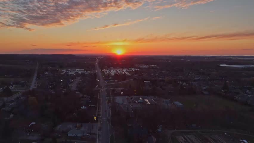 Spectacular aerial view of a city at sunset with a long highway stretching toward the glowing horizon.