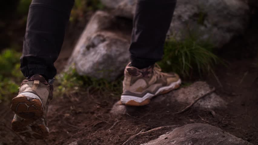 Person hiking over rocks holding camera on mountain trail
