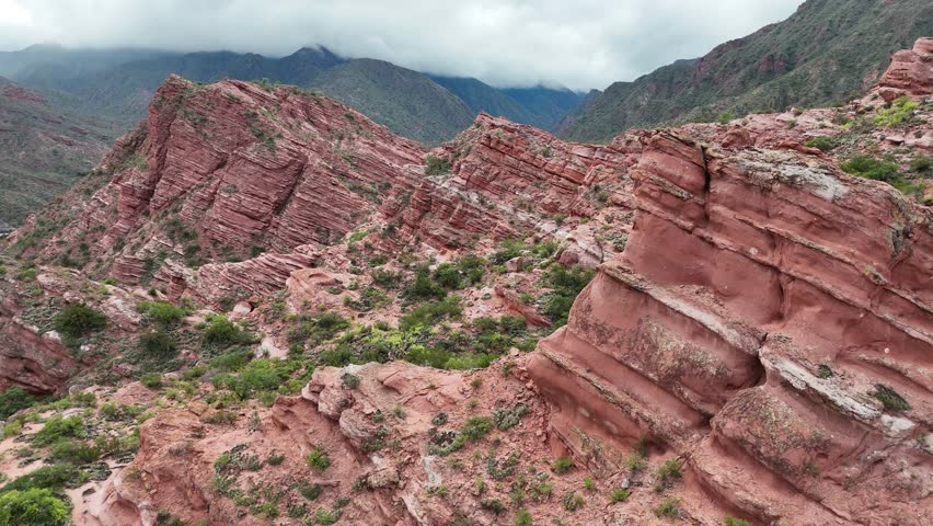 Aerial view of majestic red rock mountain formations with green vegetation under a cloudy sky.