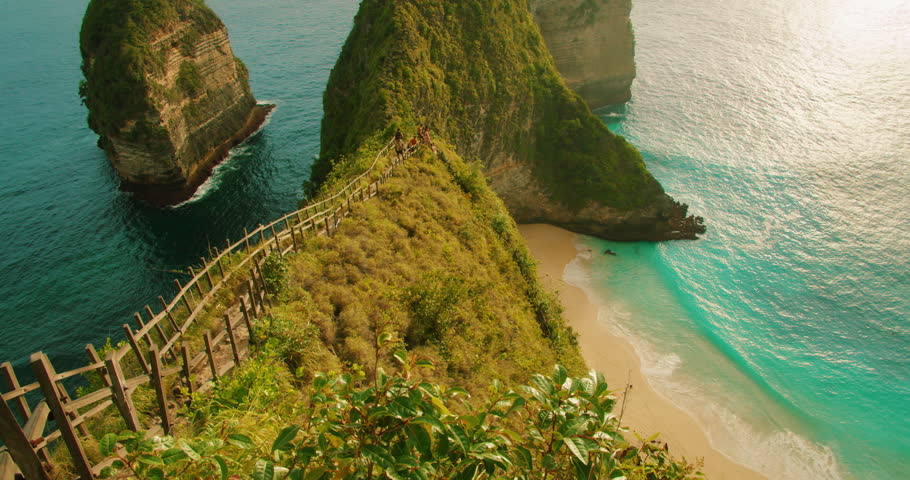 Steep wooden staircase leading down to sandy Kelingking Beach from high green cliff in Bali Nusa Penida