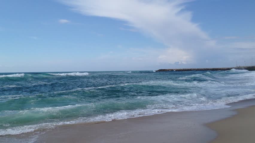Beautiful beach with ocean sea crashing rolling waves under a blue sky with white clouds, rip currents.