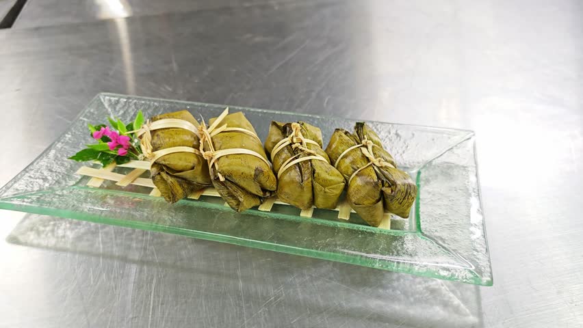 Authentic Thai dessert, Khao Tom Mat (Steamed Sticky Rice with Banana and Black Beans) wrapped in banana leaves and tied with bamboo strips.