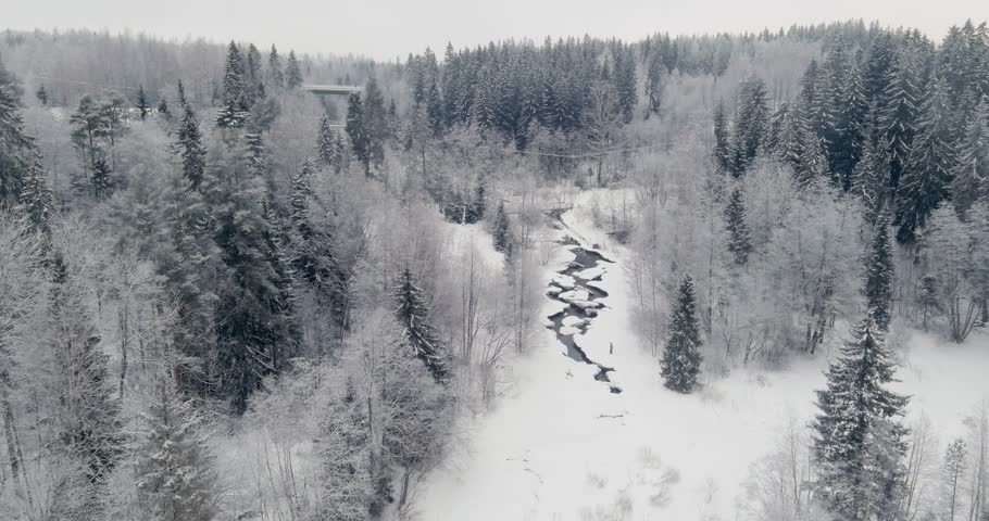 Aerial view of shows the Vantaa River flowing through a snow-covered forest at Myllykoski rapids in cloudy winter weather, Nurmijärvi, Finland, Europe.