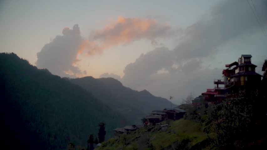 Sunset over a mountain village in India with dramatic clouds and rolling hills, capturing peaceful nature, rural life and scenic landscape.