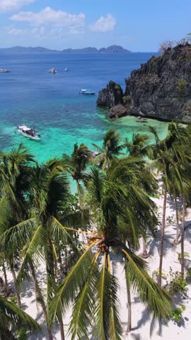 Aerial view of traditional boats in crystal clear turquoise lagoon in El Nido, Palawan, Philippines. Tropical beach, palm trees and limestone cliffs create stunning island scenery.