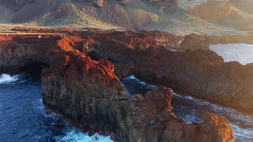 Aerial view of Arco de la Tosca natural rock arch on El Hierro island, Canary Islands, Spain. Golden sunlight illuminates the volcanic red cliffs of El Hierro island, Canary Islands, Spain
