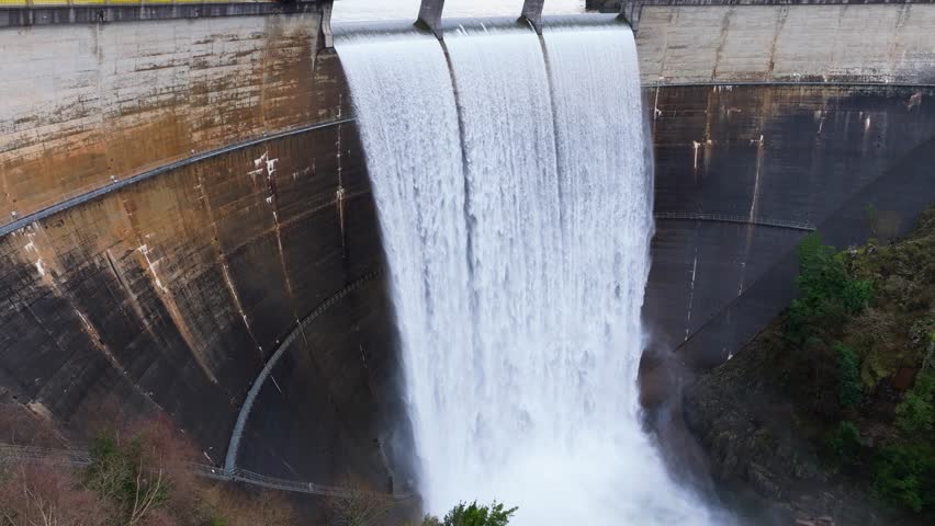 Curved Concrete Dam Spillway Releasing Powerful Torrent Of Water Into Misty Basin - Eume Reservoir, Galicia, Spain. aerial shot