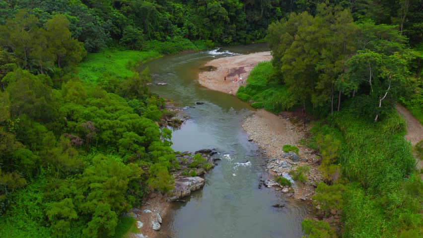 Aerial view of winding river flowing through dense tropical rainforest with rocky banks and lush vegetation