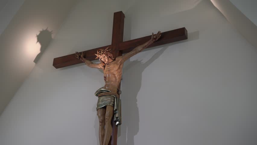 Wooden crucifix statue of Jesus Christ hanging on a white wall with a dramatic shadow
