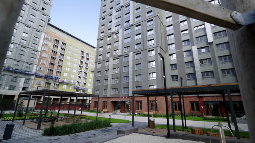 Wooden playground structure includes metal slide in sandy area. Apartment buildings provide contrasting background to natural kids zone