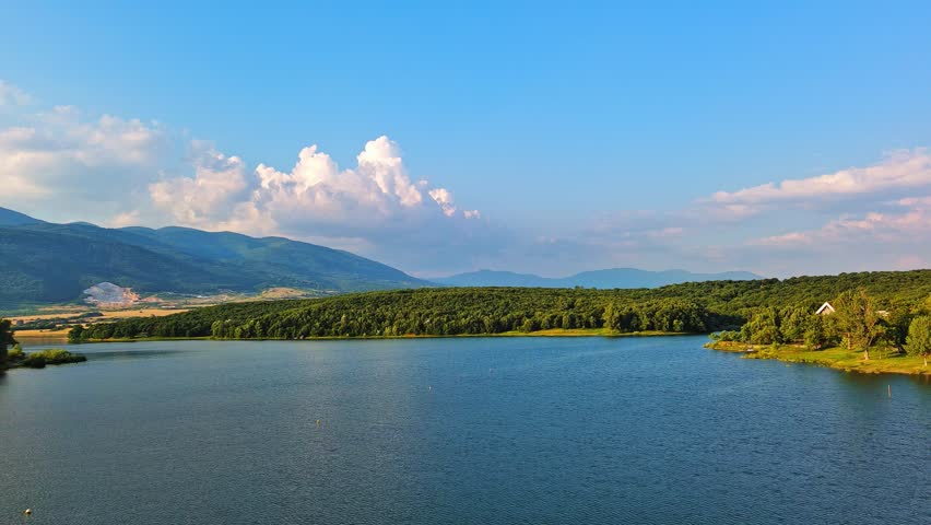 Lake with clear water and stone shore in spruce forest with fir trees against a daytime sky
