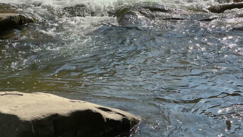 Low multi-level cascade waterfall on a small mountain river at autumn sunny day, view close-up while vertical panning
