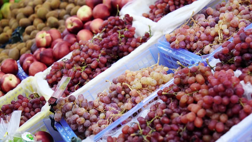 Fruit display at a market with various types of grapes, apples, and kiwis in the daytime