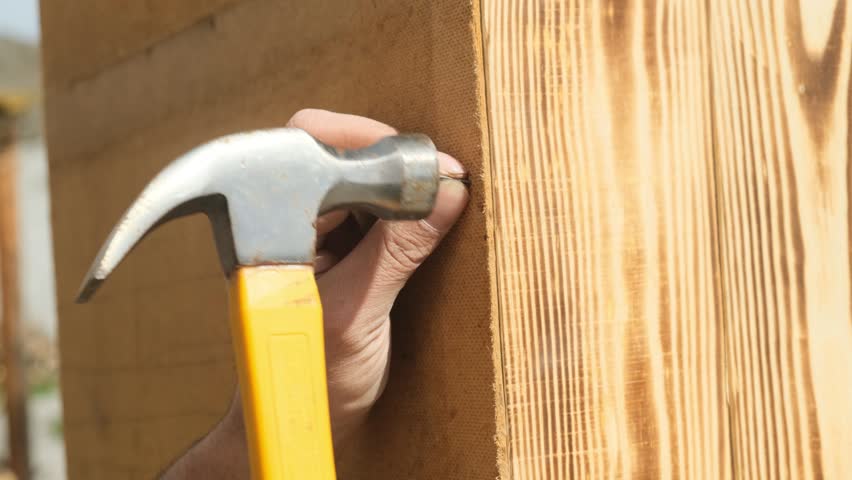 Man hands using hammer to drive nail securing back panel of wooden cabinet made of hardboard. Furniture maker assembling cabinet. Final part of wooden furniture assembly. Hammering nail.