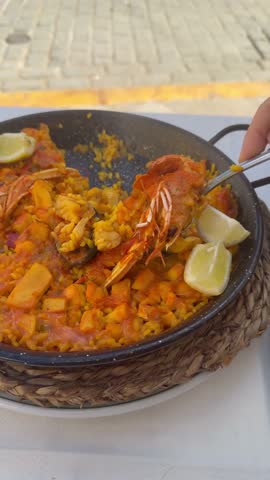 Person eating seafood paella with fork in outdoor restaurant setting during meal