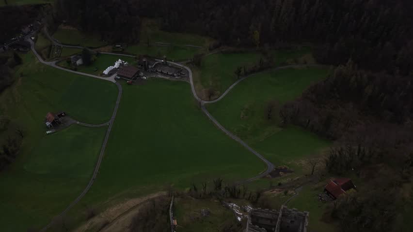 Drone flying over Swiss farm with round hay bales and agricultural roads. Rural landscape and farming activity in alpine region.