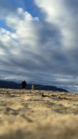 Young girl with her dad running on a sandy beach on a sunny evening in slow motion