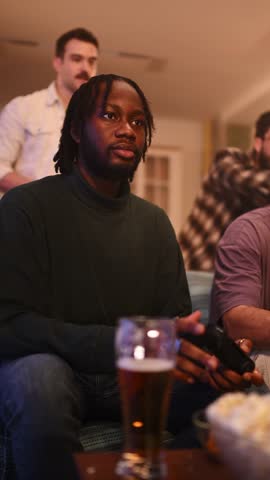 Group of diverse male friends having fun playing video games in a living room, eating popcorn and drinking beer during a social gathering