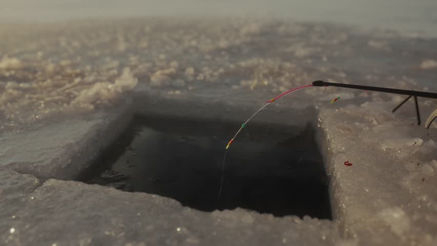 Ice fishing scene showing fishing line dropping into a hole in the ice, followed by a caught fish being pulled from the water in a snowy landscape