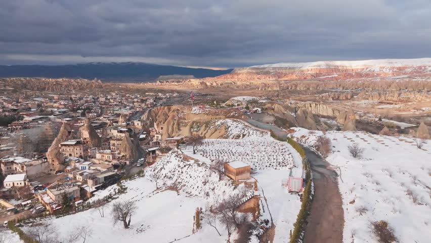 Breathtaking drone footage capturing the snowcovered fairy chimneys and ancient cave dwellings of Goreme in Cappadocia, Turkey, under a dramatic winter sky.