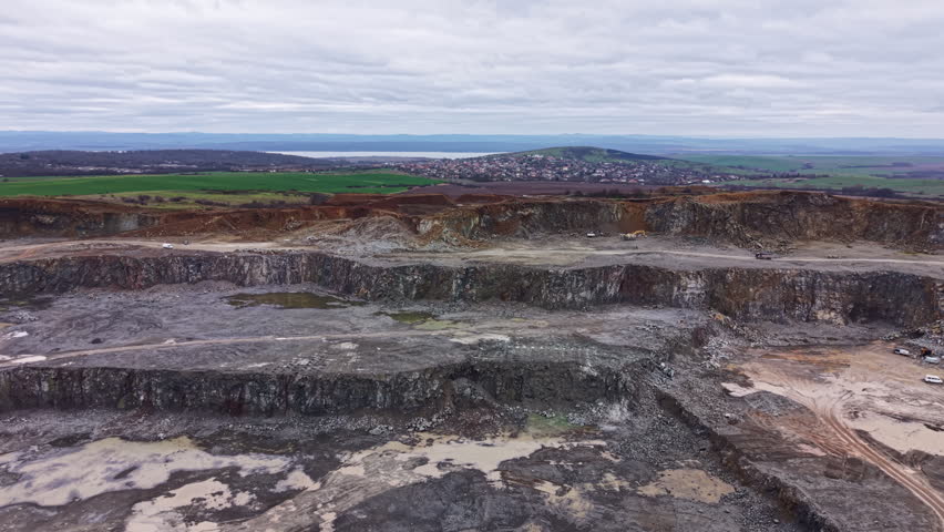 A granite quarry shows large rock formations and machinery working on the site. The landscape includes hills and greenery in the background, with clouds above.