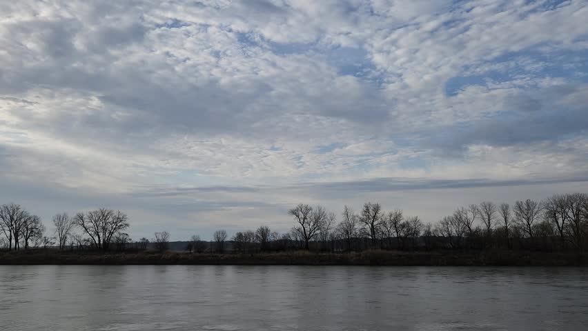 Calm river beneath expansive cloud-filled sky with subtle reflections
