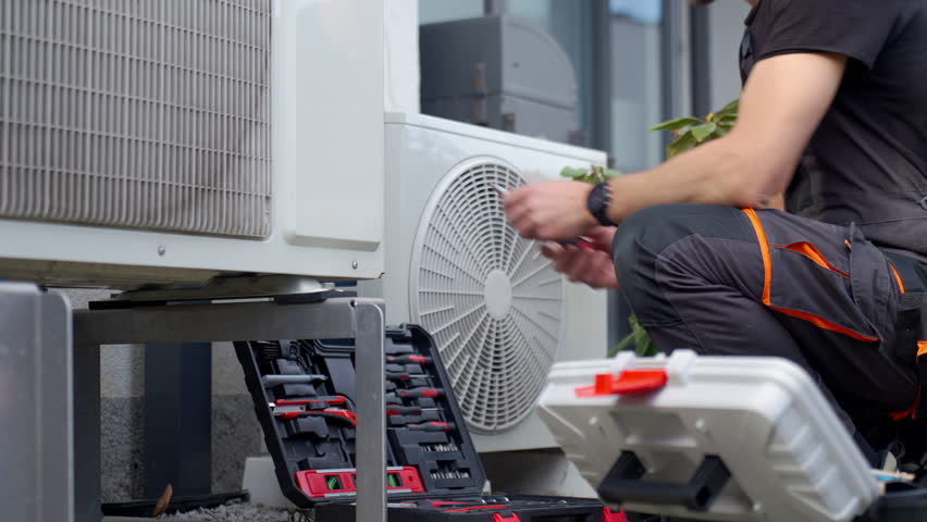 Technician servicing outdoor heat pump unit with tools beside residential house. Concept of HVAC maintenance, home climate control and energy efficient heating and cooling