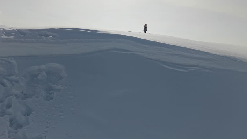 Almaty, Kazakhstan - March 28, 2026: A person stands on a snow-covered mountain, with a snowmobile nearby and trees in the background, showcasing the beautiful winter landscape and outdoor adventure