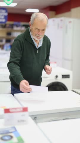Mature man choose washing machine or dishwasher at a supermarket. High quality 4k footage