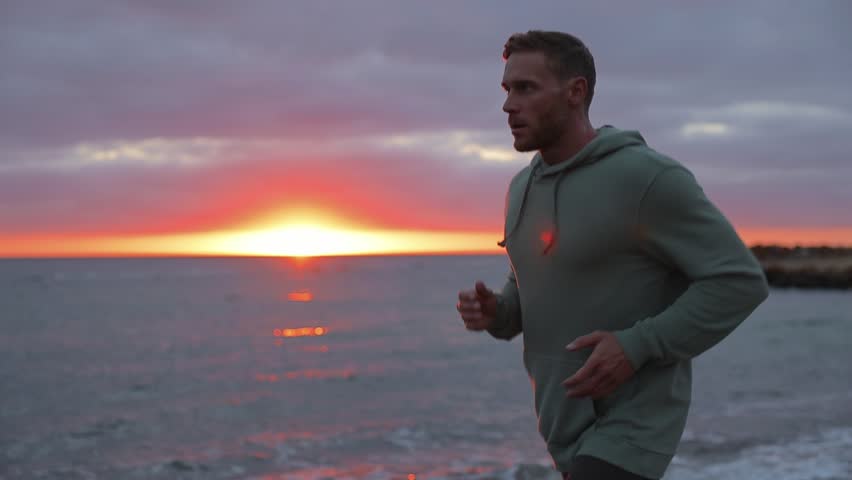 Young cool active Caucasian strong sporty athletic fit sportsman man he wear sports clothes running jogging warm up train at sunrise sun dawn over sea beach outdoor on seaside in summer day morning