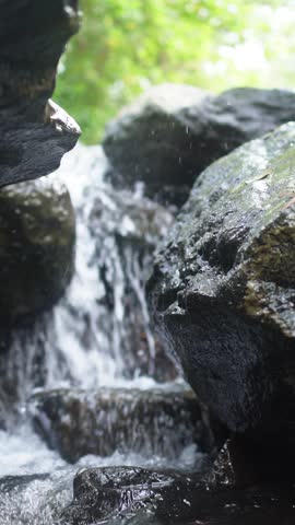 Tranquil Forest Waterfall Flowing Over Rocks With Soft Sunlight and Lush Greenery, peaceful nature vertical background. Flowing Mountain Stream Over Rocks Through Tropical Forest With Lush Green Foliage And Clear Water
