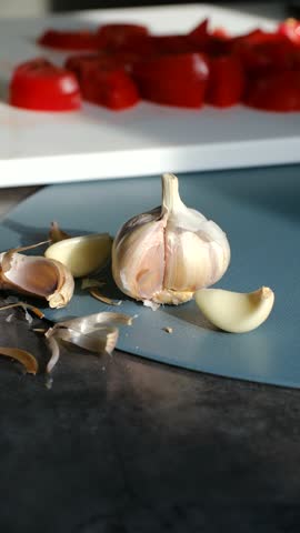 Fresh organic garlic bulb with cloves and chopped red bell pepper on cutting boards. Illuminated by natural sunlight in kitchen setting. Showcasing healthy cooking and meal preparation ingredients