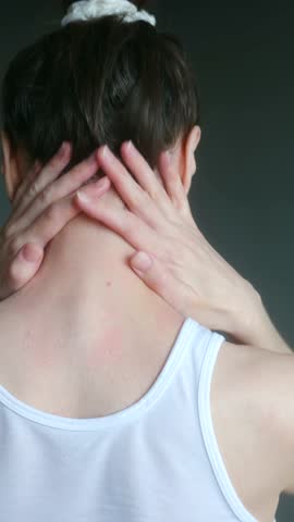 Unrecognizable woman with her hair up massaging her sore neck and shoulders, feeling tense and tired. Her muscles are stiff, and red spots from rubbing are visible on her skin. Vertical. Neck pain.