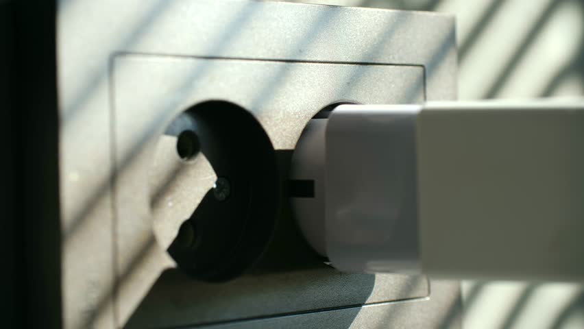 Person unplugging a white charger from a gray wall outlet to disconnect a device and save electricity, illustrating energy conservation and reducing household power consumption costs